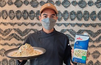 A person presenting a plated dish and an Anchor product carton.
