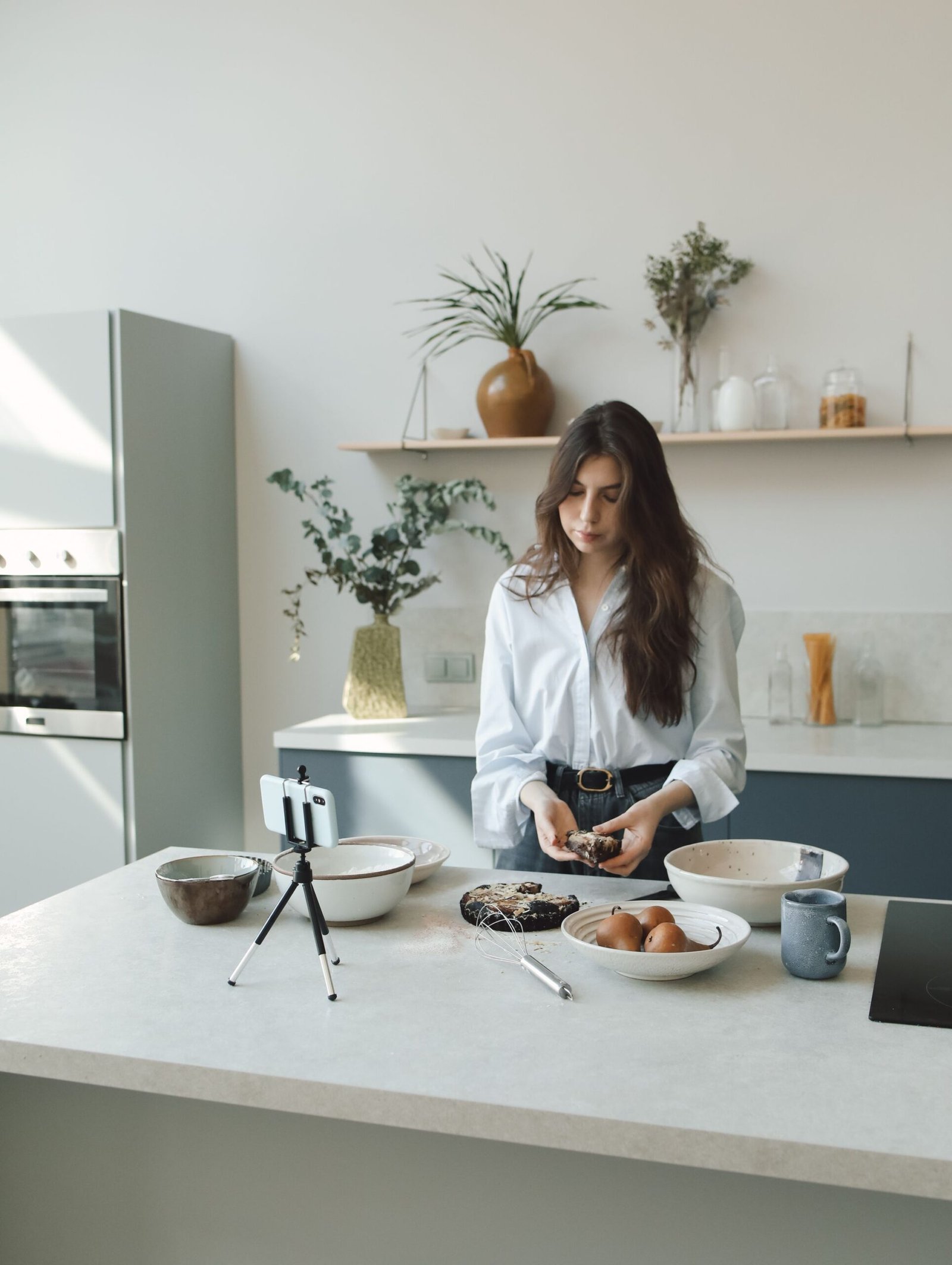 A woman demonstrating baking while recording with a smartphone on a tripod.