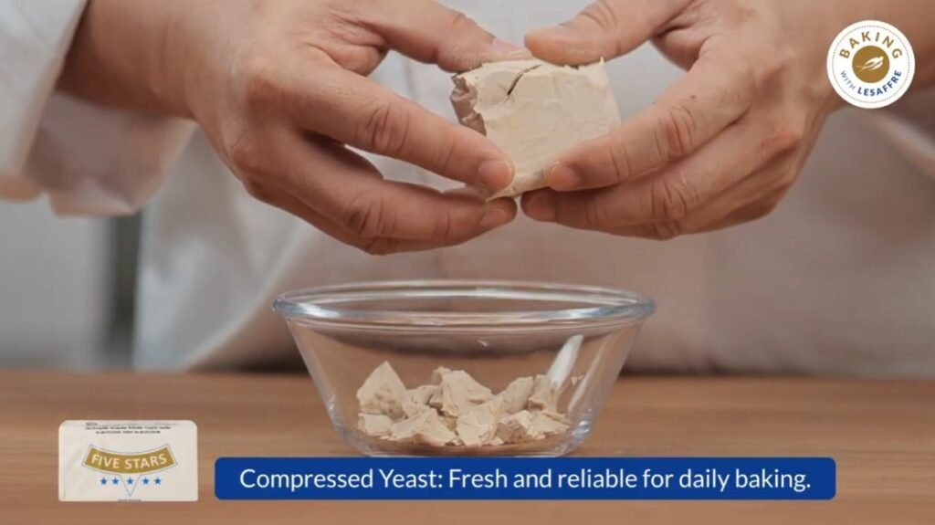 Hands crumbling fresh compressed yeast into a glass bowl